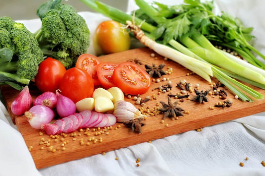 a cutting board covered in healthy food such as broccoli, celery, and garlic
