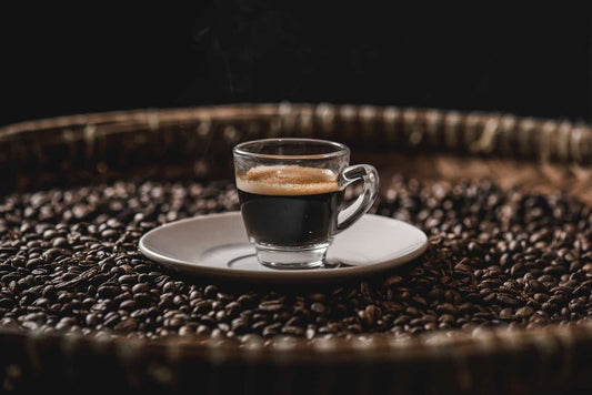 a small cup of espresso sitting on a white plate on top of roasted coffee beans